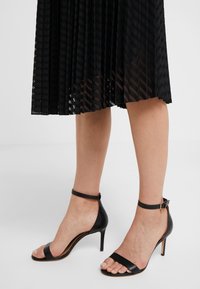 Sandali neri con tacco alto, dotati di cinturino alla caviglia, design open toe, texture in pelle liscia e sottile tacco a spillo.