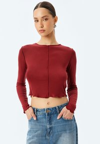 Röd kortärmad top i ribbat tyg med rundad halsringning och rå kant. Matchas med blå högmidjade jeans.