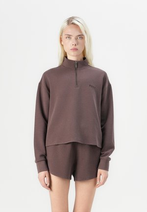 Brun zip-up genser med kort krage og teksturert stoff, kombinert med matchende brune shorts. Har en liten logo på brystet.