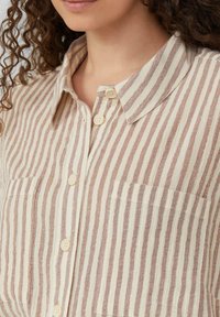 Chemise rayée beige et marron clair, avec un col, un bouton-pression à l'avant et deux poches à l'avant. Le tissu a une finition texturée.