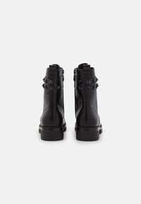 Botas de tobillo de cuero negro con una textura suave, acentos de tachuelas en el cuello y una suela de goma plana con sutiles detalles de costura.