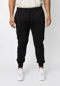 Zwarte sweatpants met een elastische tailleband en een trekkoord, voorzien van ribgebreide boorden en een zachte, gestructureerde stof. Draagt met witte sneakers.