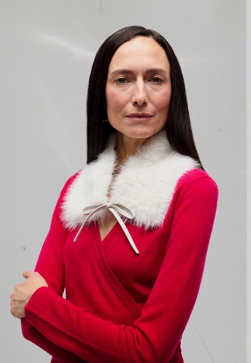Pulover roșu tip învelitoare cu un guler moale din blană albă, legat cu o panglică gri deschis, având mâneci lungi și un decolteu în V.