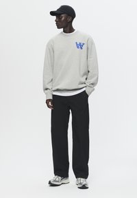 Hanorac gri cu un logo albastru, șapcă neagră, pantaloni largi negri și adidași gri cu accente albe și albastre.