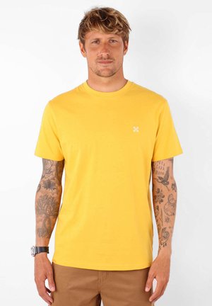 T-shirt jaune à manches courtes en coton, avec col rond. Comprend un petit détail de logo blanc sur la poitrine. Texture lisse.