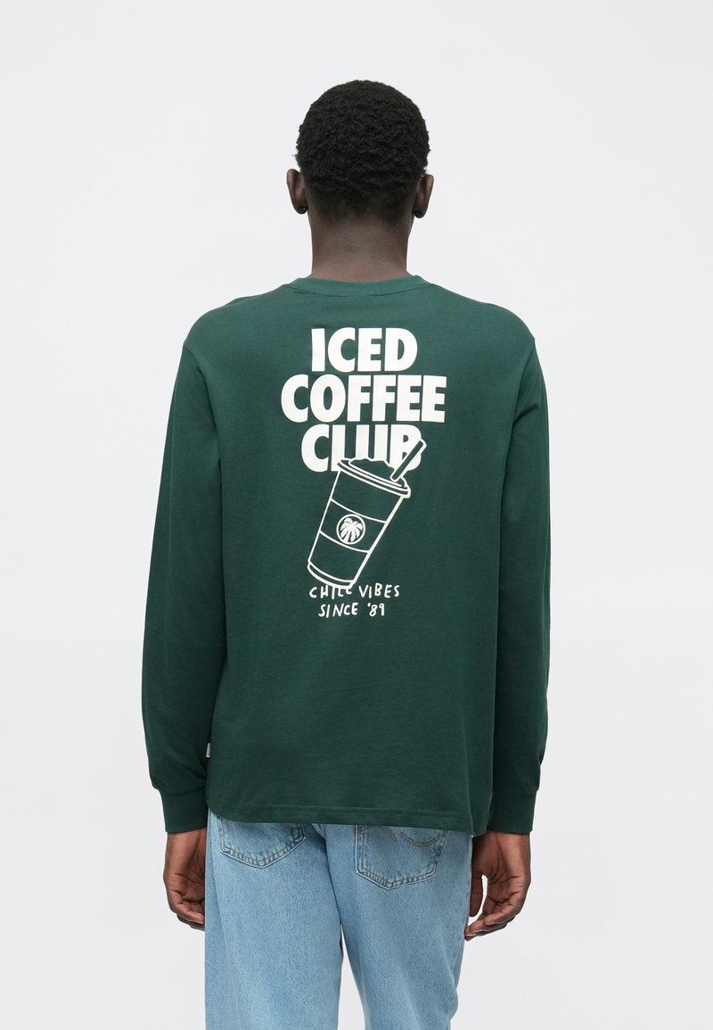 Zelena majica dugih rukava s grafičkim printom na leđima koji sadrži tekst "ICED COFFEE CLUB" i ilustraciju šalice.
