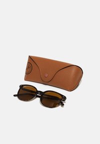 Occhiali da sole tartaruga nera con lenti rotonde posizionati accanto a un astuccio in pelle marrone testurizzata con chiusura a scatto.