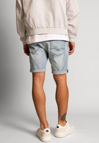 Șorturi din denim de culoare albastru deschis, cu margini răsucite, două buzunare pe spate cu modele cusute, purtate cu o jachetă deschisă și adidași albi.