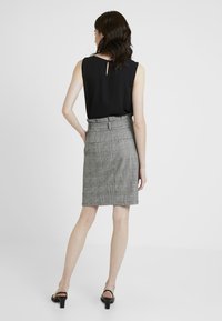 Haut sans manches noir avec dos en clé, associé à une jupe crayon à carreaux gris avec passants de ceinture et coupe slim. Sandales à talons noires.