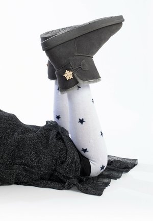 Botines de ante gris con un acento de copo de nieve, combinados con calcetines blancos con estrellas marinas. Tela negra texturizada visible en el fondo.