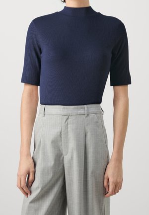 Haut bleu marine à manches courtes avec col montant, assorti à un pantalon large à fines rayures gris clair taille haute sur fond neutre.