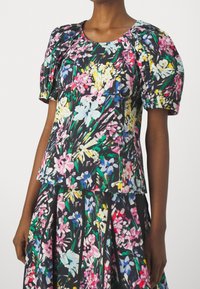 Top floreale a maniche corte con sfondo nero, caratterizzato da vivaci fiori rosa, blu e gialli, e maniche a sbuffo gatherate per un tocco di texture in più.