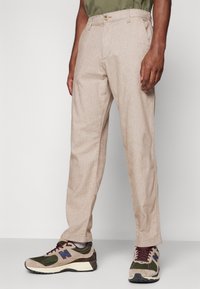 Beige linen trousers with a straight fit, featuring side pockets and a button closure. Worn with multicolored athletic shoes.
