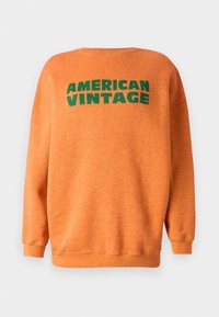 Ruskih oranžova majica s dugim rukavima i okruglim izrezom. Ispred se nalazi veliki zeleni natpis "AMERICAN VINTAGE". Mekana tekstura.