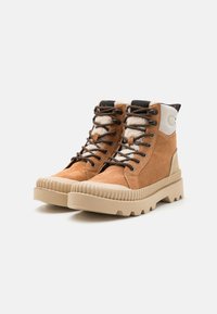 Bottes de randonnée en daim marron avec une semelle beige nervurée, dotées de lacets noirs et d'un accent beige au niveau du talon, un col en tissu texturé et une construction durable.