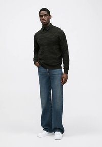 Pull texturé noir, jean bleu coupe décontractée et baskets blanches. La tenue présente un col classique et une silhouette simple.