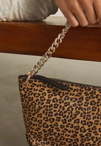 Handtas met luipaardprint, gemaakt van zacht materiaal, met een gouden schouderriem, een bovenrits en zwart leren afwerking langs de opening.