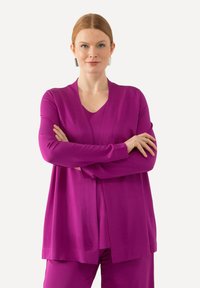 Langärmlige, offene Strickjacke und passendes Oberteil in leuchtendem Magenta. Glatte Textur mit lockerer Passform, ohne sichtbare Verschlüsse.