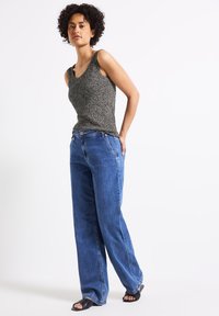 Černobílý tank top se vzorem, v kombinaci s volnými modrými džínami. Ploché černé sandály dotvářejí vzhled. Minimalistický styl, uvolněný střih.