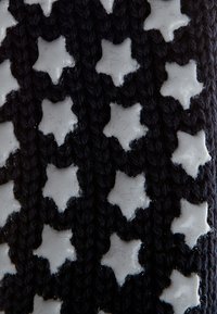 Tejido negro de punto que presenta formas estrelladas en relieve en blanco. La textura es áspera con un diseño decorativo y flexible.