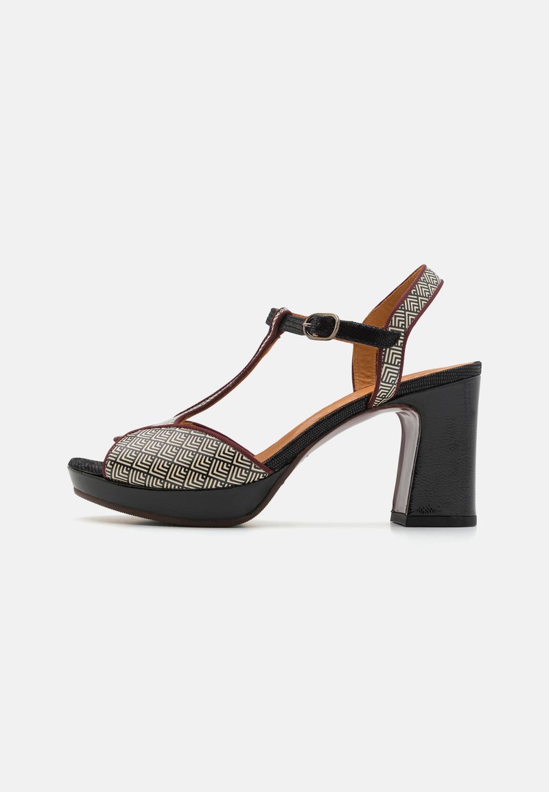 T-strap high-heeled shoe in black and geometric patterned fabric. Features a chunky heel and adjustable ankle strap.