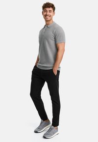 Polo gris de manga corta con cuello, combinado con pantalones negros ajustados y zapatillas grises. Diseño simple con una textura suave.