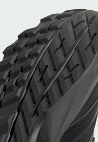 Čierna atletická podrážka topánky s robustným vzorom tread, hlbokými ryhami a rôznymi textúrami pre trakciu a odolnosť.