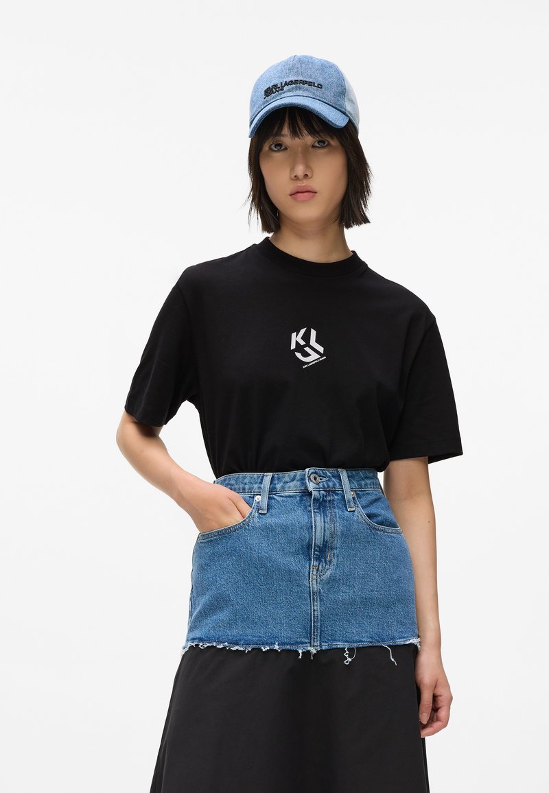 Tricou negru din bumbac cu un logo alb, asociat cu o fustă din denim albastru. Outfitul este completat cu o șapcă de baseball albă.
