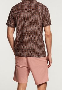 Koszula z krótkim rękawem na ciemnym tle z wzorem liści w kolorze pomarańczowym, zestawiona z jasnoróżowymi szortami, prezentując luźny krój.