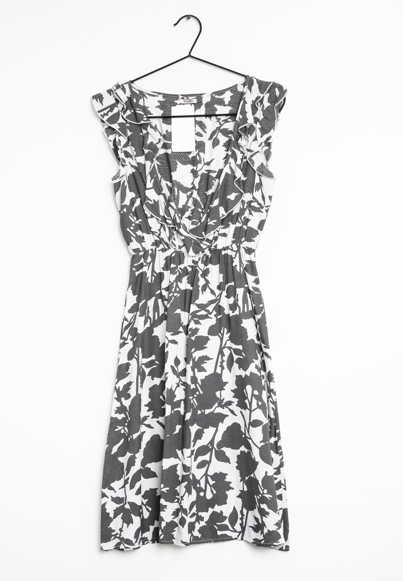 Robe sans manches noire et blanche à motifs floraux avec épaules volantées et col en V, suspendue sur un cintre noir sur fond blanc.