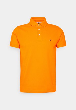 Polo arancione in cotone, con colletto, tre bottoni bianchi, maniche corte e un piccolo logo sul lato sinistro del petto.