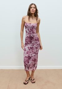 Robe slip à imprimé floral violet avec des bretelles fines, silhouette moulante et tissu doux et fluide. Portée avec des sandales à talons noirs.