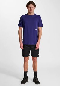 Maglietta sportiva viola a maniche corte con un piccolo logo, abbinata a pantaloncini neri. La maglietta ha uno scollo rotondo e una texture liscia.