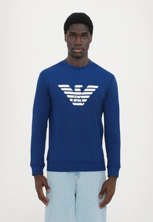 Sudadera azul con mangas largas, que presenta un logo gráfico blanco en el pecho. Fabricada con una suave tela de punto y con cuello redondo.