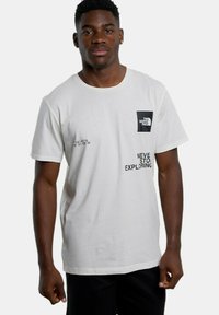 Camiseta de algodón blanca con un parche negro con el logo, texto impreso "NUNCA DEJES DE EXPLORAR" y coordenadas geográficas en negro. Mangas cortas.