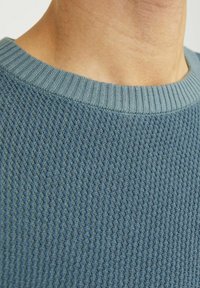 Teksturowany niebieski sweter z prążkowanym okrągłym dekoltem. Materiał ma wzór tkaniny i miękką, oddychającą teksturę.