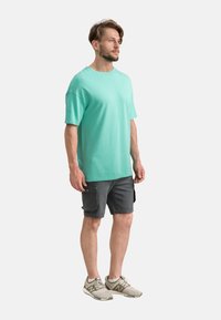 T-shirt en coton vert menthe, coupe décontractée ; associé à un short cargo gris foncé avec poches latérales ; chaussures de sport grises.