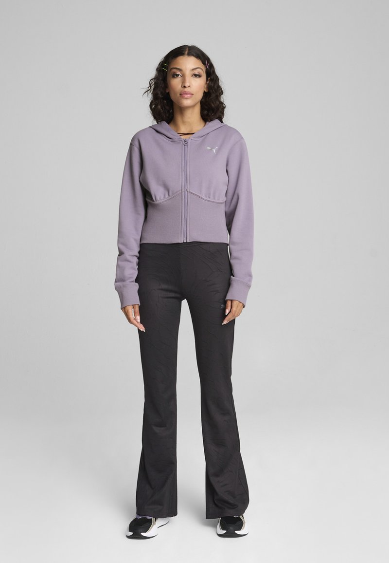 Felpa viola corta con zip e cappuccio, abbinata a pantaloni neri a campana con un motivo testurizzato, completata con sneaker bianche e nere.