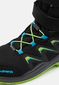 Stivale da trekking nero con lacci verdi e blu, caratterizzato da una tomaia in tessuto testurizzato e un'etichetta Gore-Tex. Suola in gomma resistente con design sagomato.