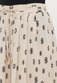 Beige skirt with black geometric patterns, pleated design, and a drawstring waist. Lightweight fabric with a smooth texture.