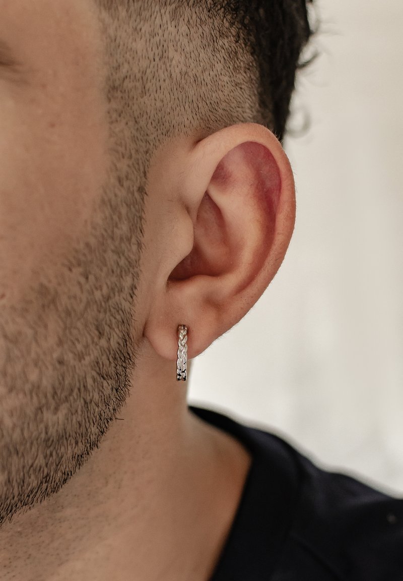 Hängende Ohrringe aus Sterlingsilber mit geflochtenem Design, das eine glänzend polierte Oberfläche und feine Rillen zeigt. Am linken Ohr getragen.