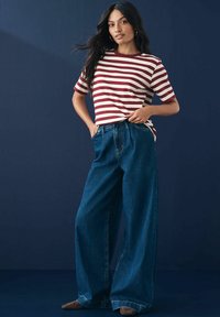 Gestreiftes T-Shirt mit kurzen Ärmeln in Creme und Kastanienbraun, kombiniert mit lässigen, irgendwo lockeren Denim-Jeans. Der Hintergrund ist in Marineblau.
