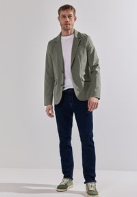 Blazer verde claro de tela suave, llevado sobre una camiseta blanca. Combinado con jeans azul oscuro y zapatillas verdes.