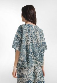 Oversized top lavet af tekstureret bomuld med et blåt og cremegult bladmotiv, brede ærmer og en nøglehulslukning på ryggen.