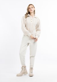 Maglione lavorato a maglia color crema con colletto, tre bottoni e polsini a costine, abbinato a pantaloni tapered beige chiaro e stivaletti beige con lacci.