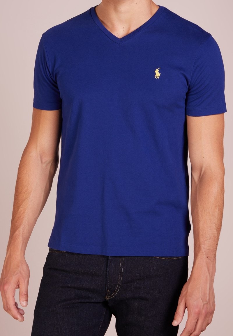 V-ringad t-shirt för män i kunglig blå bomull. Har korta ärmar och en liten gul logotyp på vänster bröst. Slät textur.