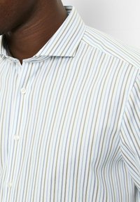 Weißes Hemd mit Knopfleiste, das dünne blaue und grüne vertikale Streifen aufweist, mit einem Kragen und einer glatten Stofftextur.