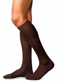 Brązowe skarpetki do kolan wykonane z gładkiego, jednolitego materiału z prążkowanymi mankietami oraz wzmocnionym palcem. Logo marki jest widoczne na podeszwie.