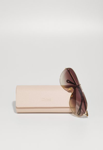 Pruunide gradient-prillide raami kuldsete detailidega, mis asuvad helesinise tekstuuri ja "Chloé" embosseeritud logoga tootal.