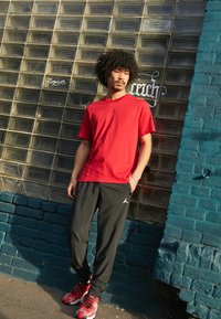 T-shirt vermelho de manga curta com um pequeno logótipo preto, combinado com calças de atletismo pretas com um logótipo e sapatilhas vermelhas com acentos pretos.